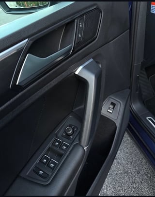 Car door interior panel showing window control buttons, door handle, and speaker grille in dark gray and black