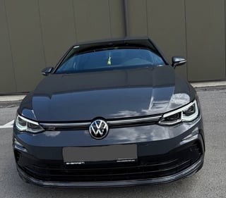 Front view of a black Volkswagen Golf electric car parked against a gray wall