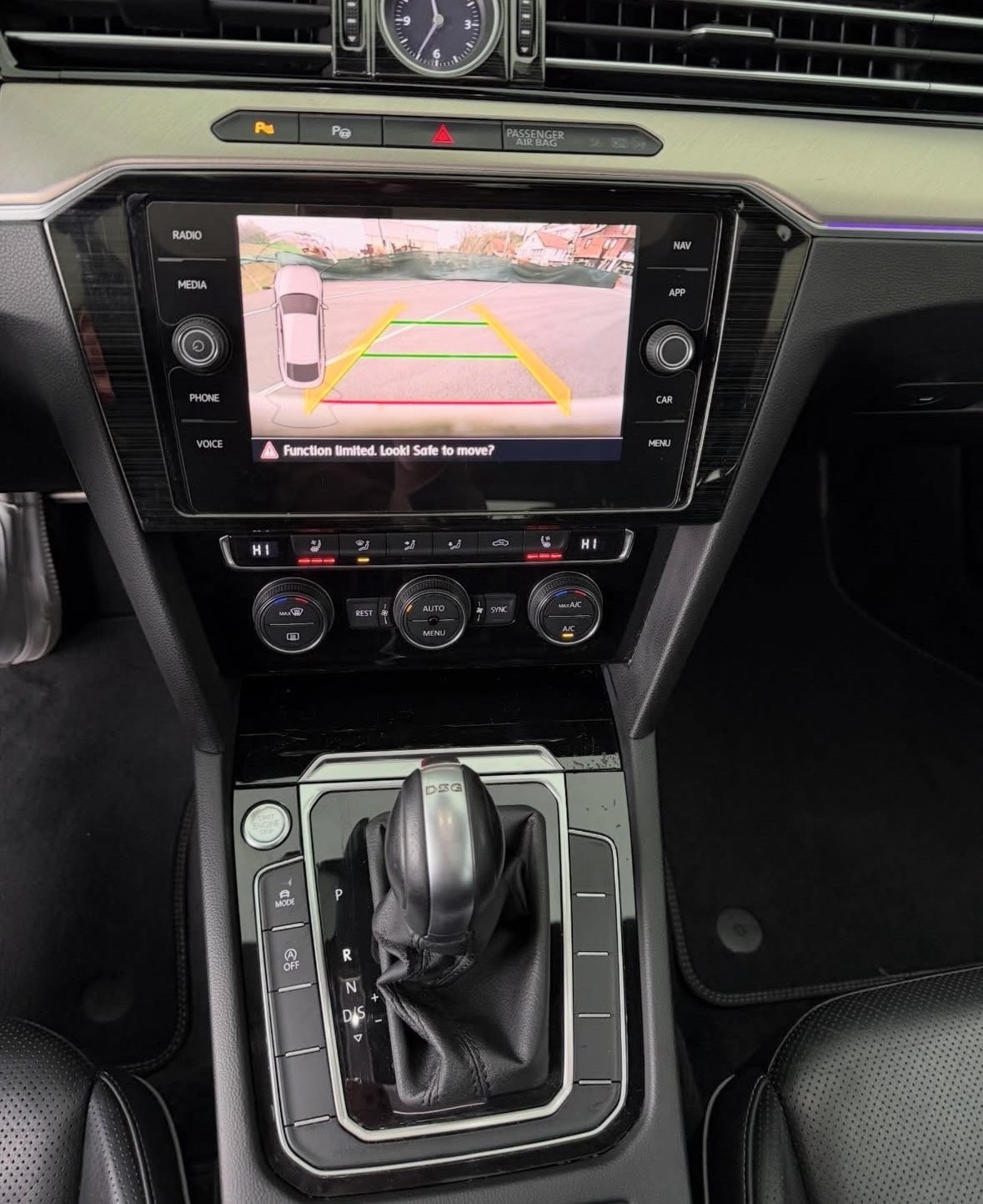 Car dashboard with touchscreen display showing rear-view camera feed and yellow parking guidelines during reversing