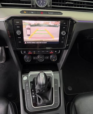 Car dashboard with touchscreen display showing rear-view camera feed and yellow parking guidelines during reversing