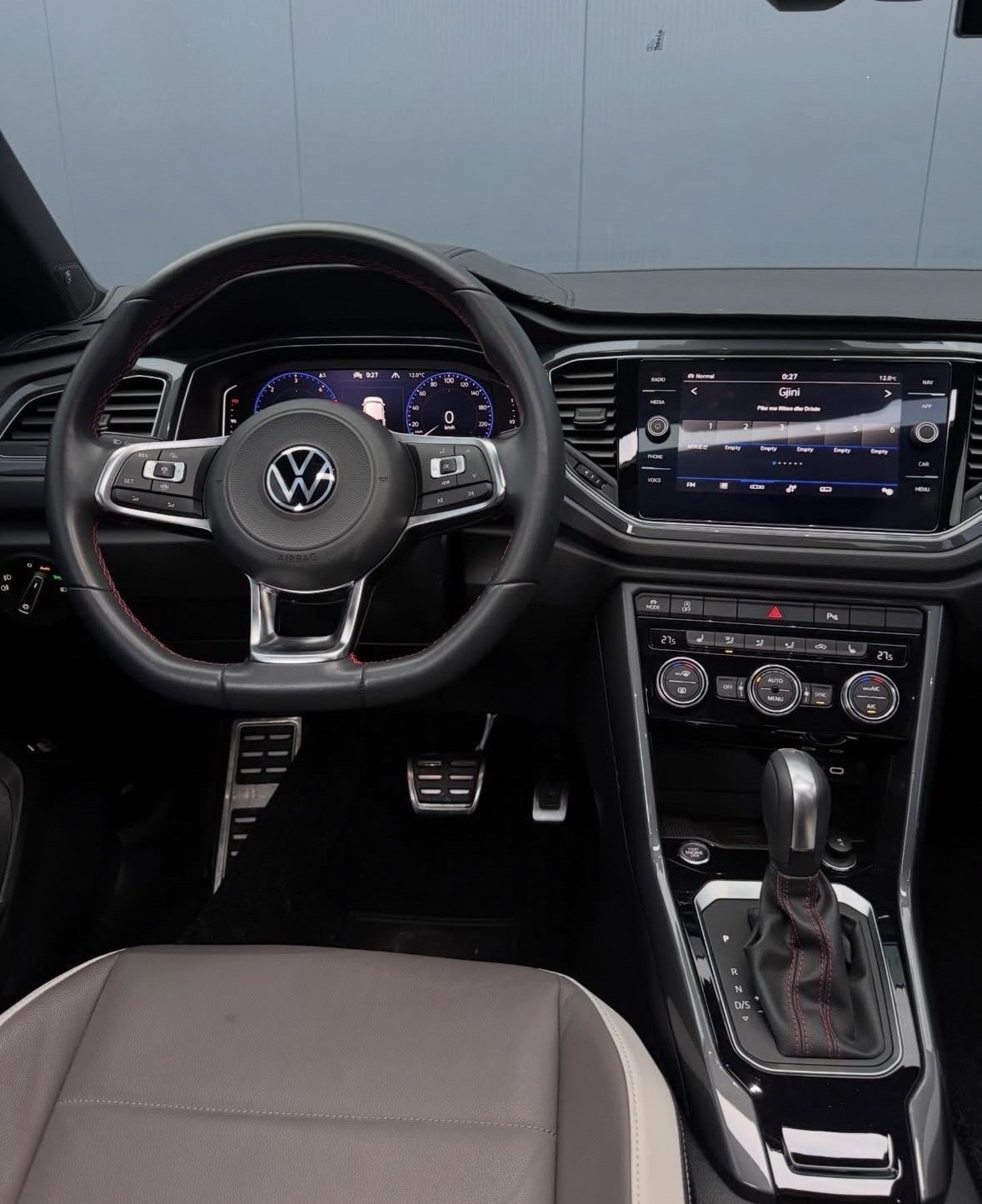 Volkswagen car interior showing steering wheel, digital dashboard display, touchscreen infotainment system, and automatic transmission shifter
