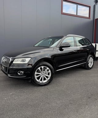 Black Audi Q5 SUV parked in front of gray industrial building with metal siding