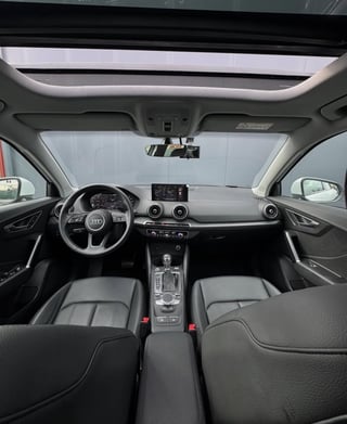 Interior view of a modern car dashboard and steering wheel with panoramic sunroof, showing black leather seats and infotainment system