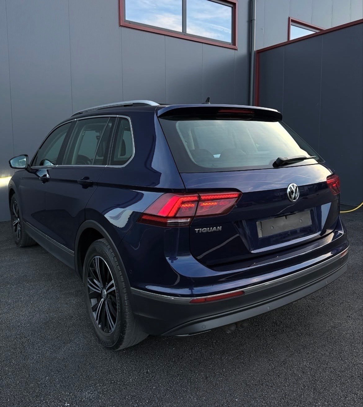Dark blue Volkswagen Tiguan SUV parked in a garage, rear three-quarter view showing red taillights and chrome trim
