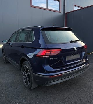 Dark blue Volkswagen Tiguan SUV parked in a garage, rear three-quarter view showing red taillights and chrome trim