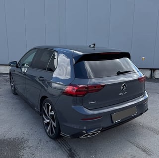 Dark blue Volkswagen Golf hatchback parked against a gray corrugated metal wall