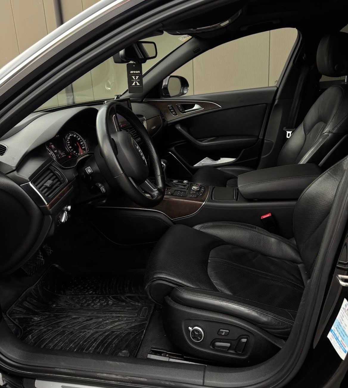Black leather car interior with steering wheel, dashboard, and open driver door visible