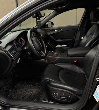Black leather car interior with steering wheel, dashboard, and open driver door visible
